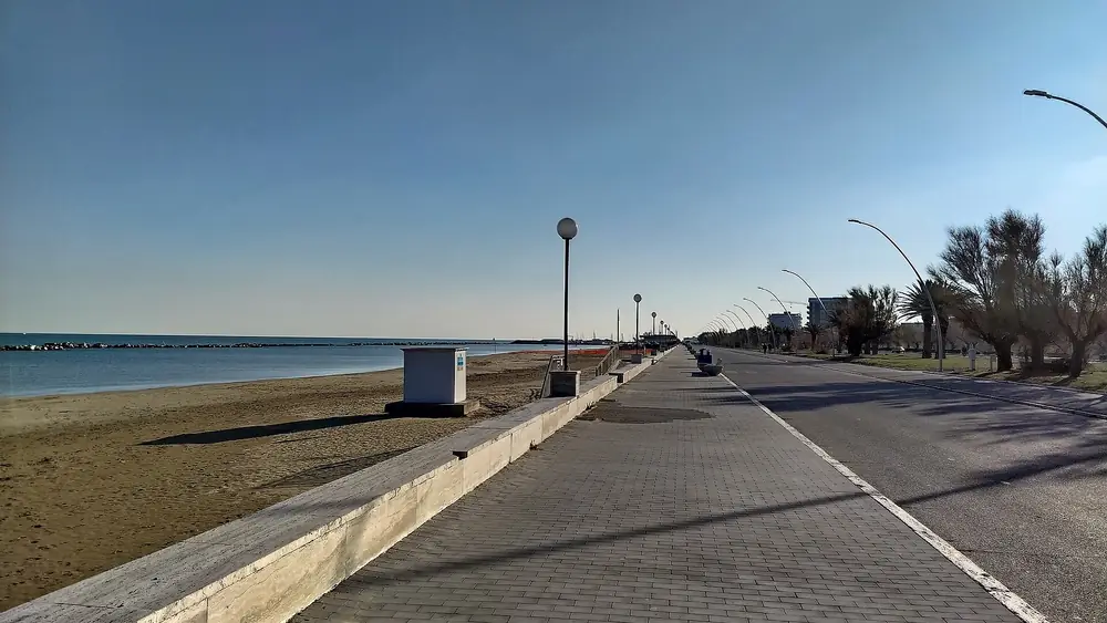 Un lungomare vuoto con una spiaggia sabbiosa e un cielo blu senza nuvole.