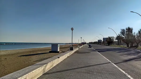 Un lungomare vuoto con una spiaggia sabbiosa e un cielo blu senza nuvole.