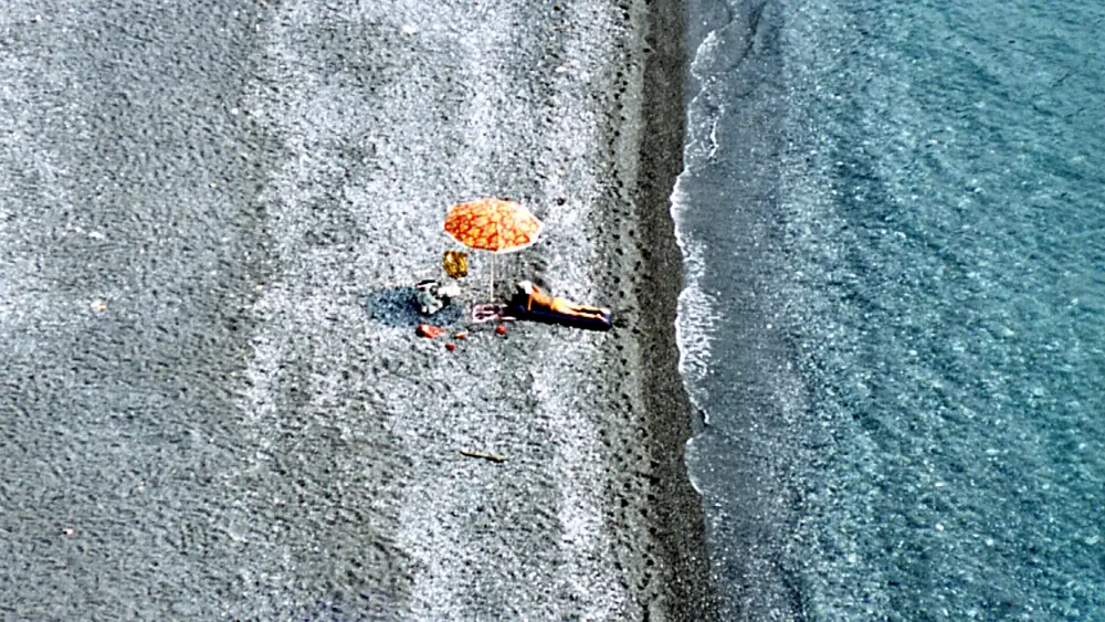 Due persone su una spiaggia con un ombrellone arancione.