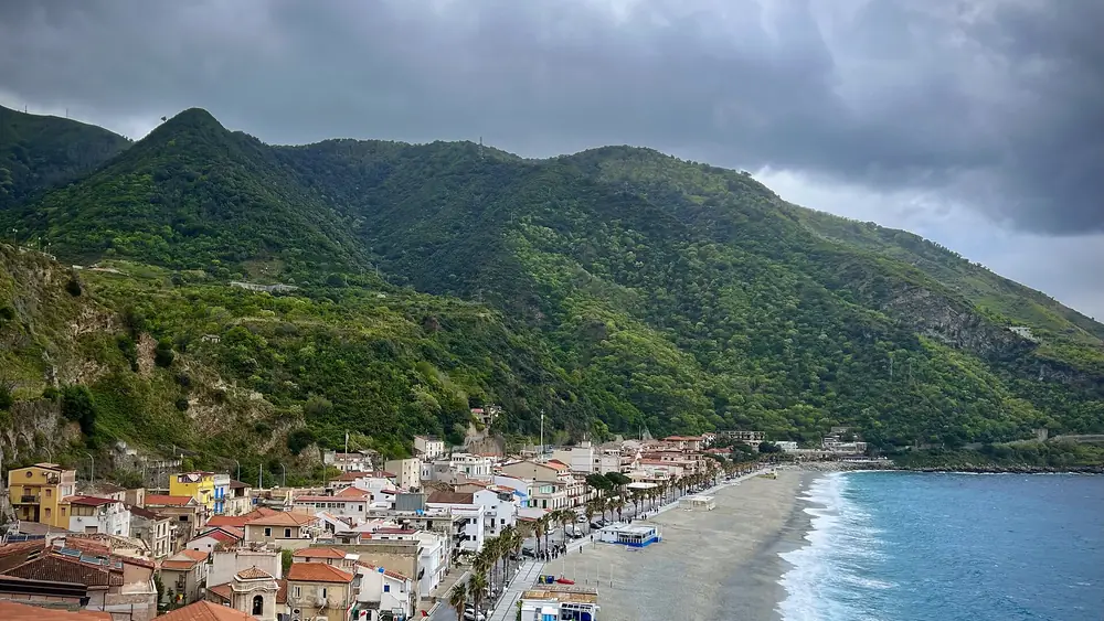 Paesaggio costiero con montagne verdi e una spiaggia vicino a una città