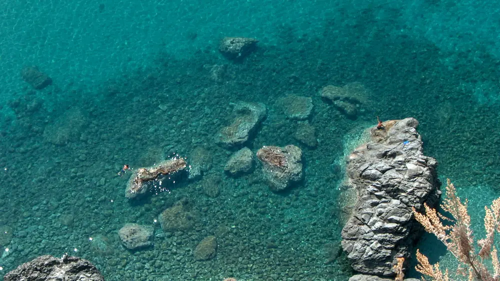 Riflessi di rocce nel mare cristallino con persone che nuotano vicino alle rocce.