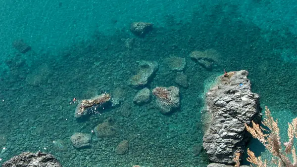 Riflessi di rocce nel mare cristallino con persone che nuotano vicino alle rocce.