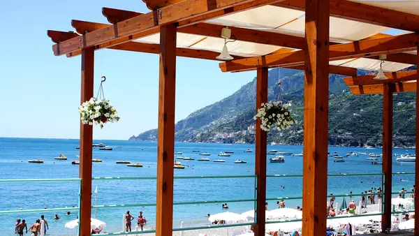 Spiaggia con persone che nuotano e prendono il sole, vista dallo spazio coperto con fiori bianchi appesi.