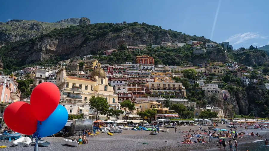 Spiaggia di Positano con balocchi rossi e blu, barche e persone che si godono il sole.