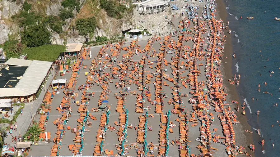 Spiaggia di Positano con molti lettini arancioni e ombrelloni, persone che si godono il sole e il mare.