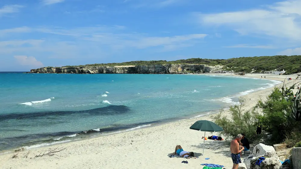Spiaggia con acqua cristallina e cielo blu, persone che si rilassano sulla sabbia.