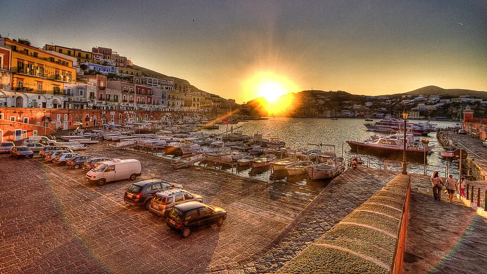 Un tramonto splendido sul porto con barche e auto parcheggiate.