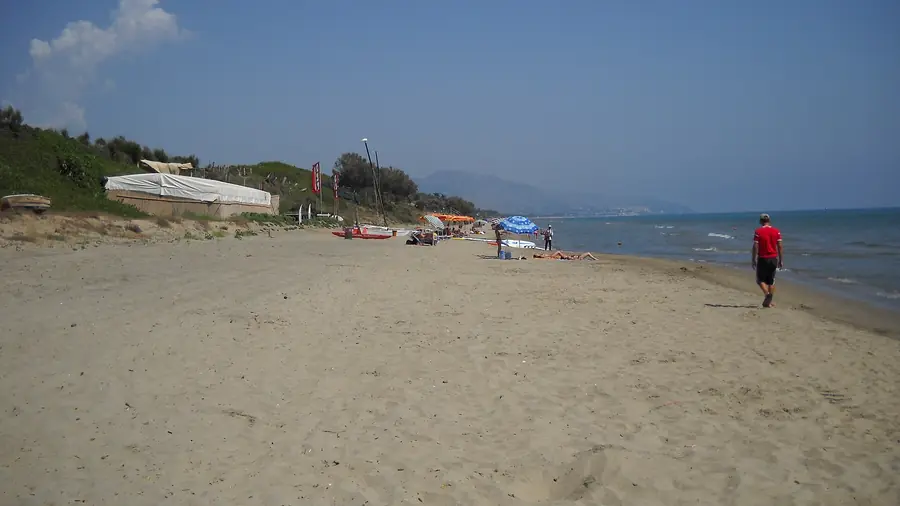 Spiaggia deserta con persone che si rilassano e barche ormeggiate sulla sabbia.