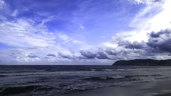 Cielo nuvoloso sopra il mare con una collina sullo sfondo.
