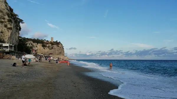 Spiaggia con persone che camminano lungo la riva e una torre sulla scogliera
