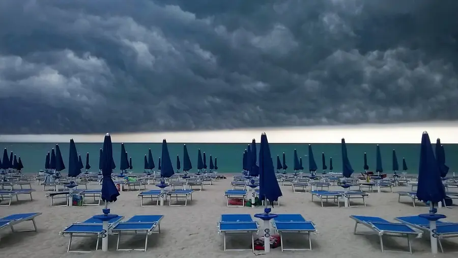 Spiaggia deserta con ombrelloni blu e nuvole scure sul cielo