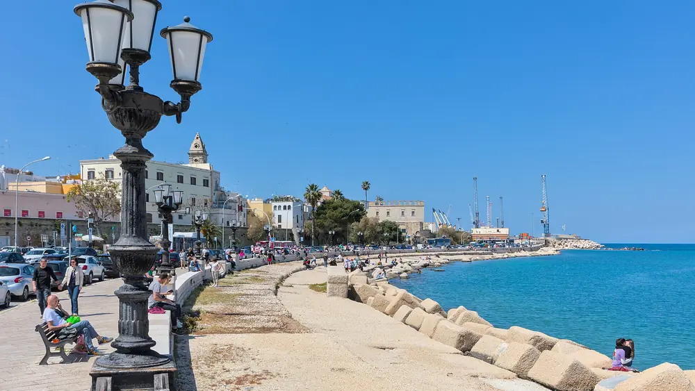 Un lungomare con persone che si godono il tempo libero, lampade da strada e una vista sul mare.