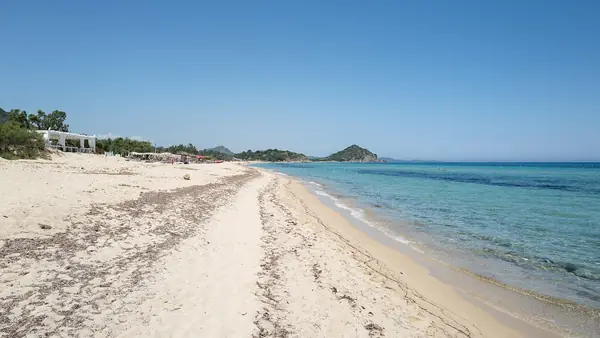 Spiaggia panoramica con sabbia bianca e acqua cristallina, sotto un cielo blu sereno.