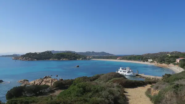 Spiaggia con acqua turchese e cielo blu, con una barca in riva al mare.