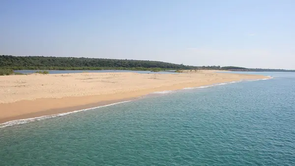 Spiaggia con sabbia dorata e acqua turchese, con un paesaggio verde sullo sfondo.