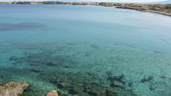 Vista panoramica di una spiaggia con acqua cristallina e roccia sullo sfondo.