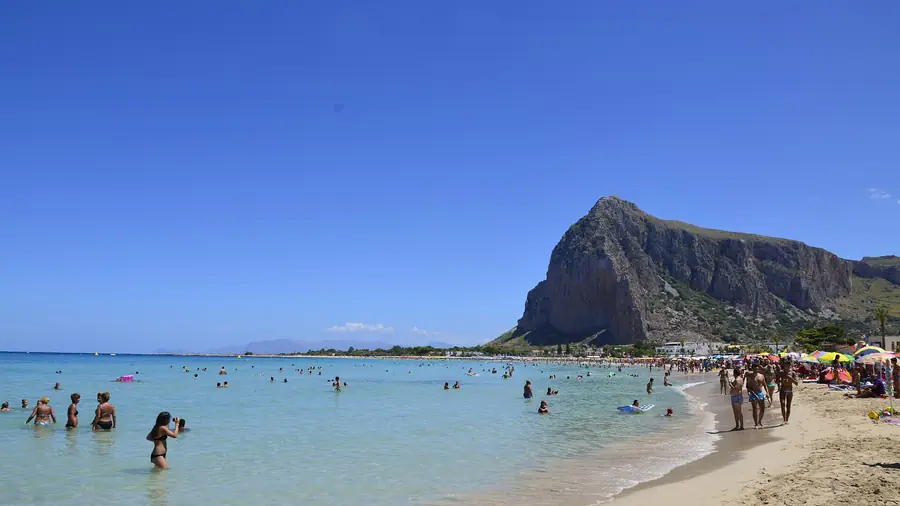 Spiaggia di San Vito Lo Capo con il Monte Monaco sullo sfondo e molti turisti che si divertono nel mare cristallino.