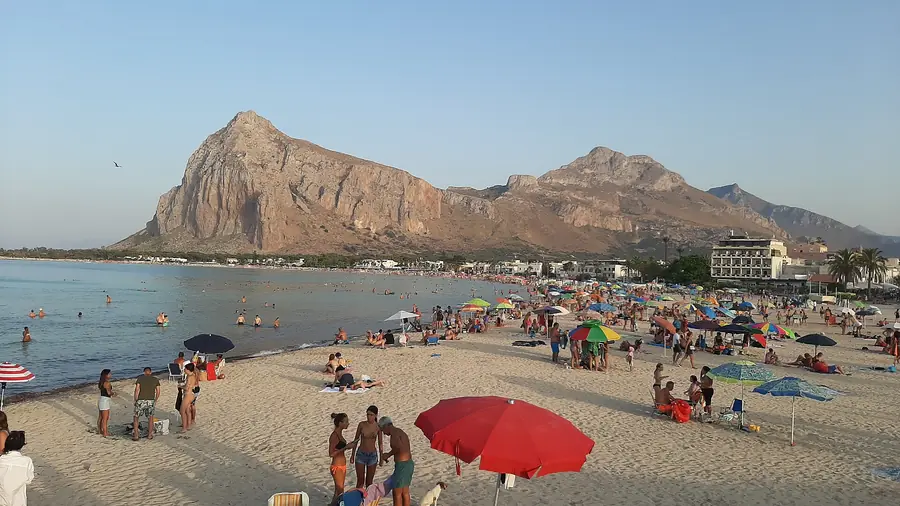 Spiaggia di San Vito Lo Capo con molti turisti e colorati ombrelloni, il Monte Monaco sullo sfondo.