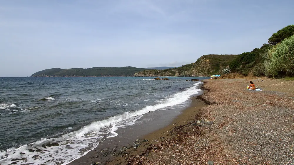 Spiaggia con acqua cristallina e cielo blu, persone che si rilassano sulla sabbia.