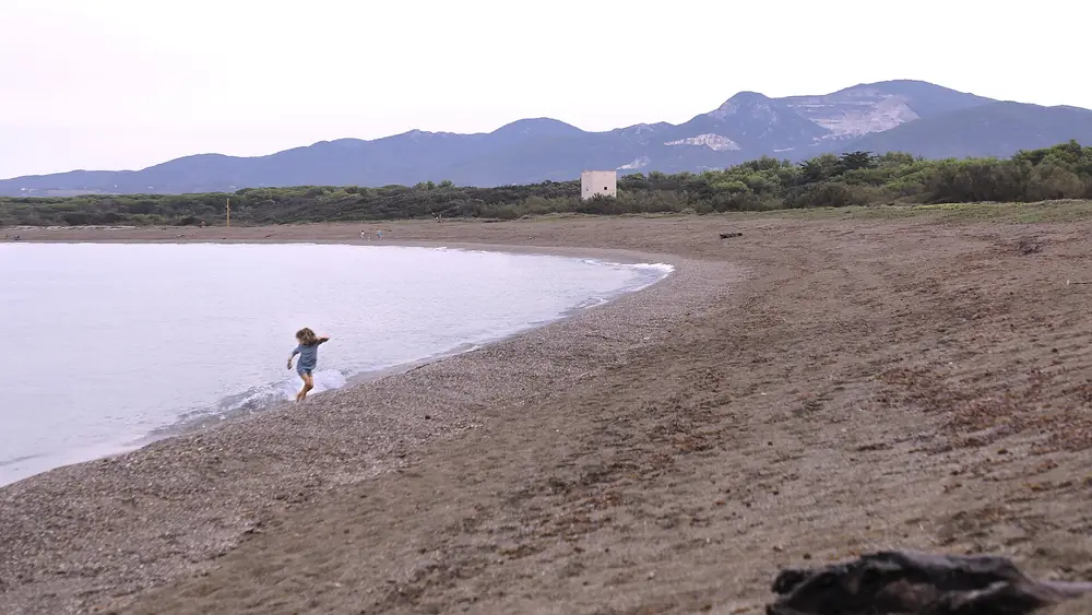 Bambina che corre sulla spiaggia con montagne sullo sfondo