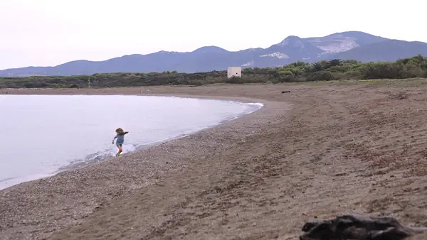 Bambina che corre sulla spiaggia con montagne sullo sfondo